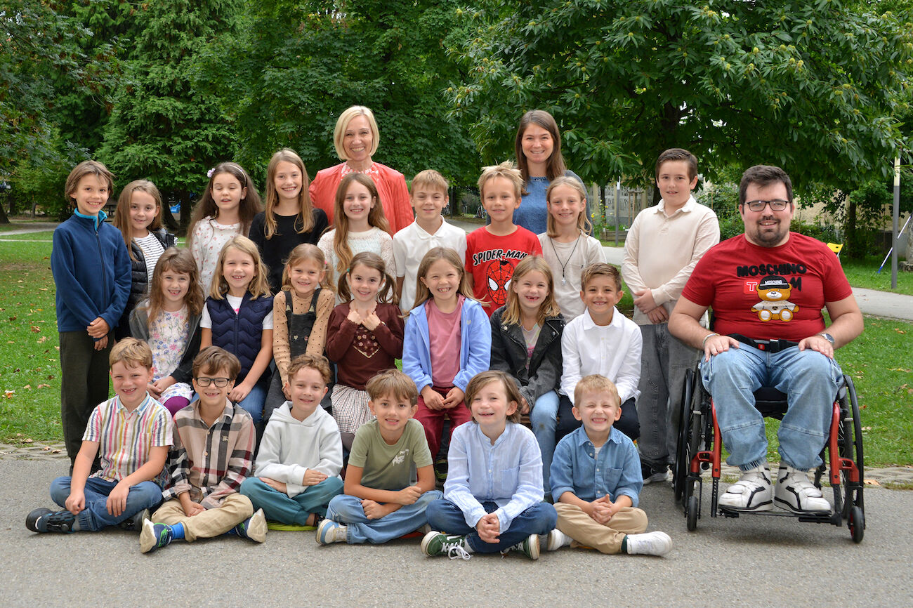 Eine Gruppe von Kindern, ein Lernbuddy und zwei Lehrpersonen posieren an einem sonnigen Tag im Freien für ein Klassenfoto.