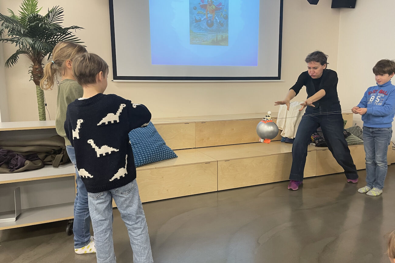 Vor einer Leinwand wird mit Hilfe von Kindern und einer Erwachsenen eine Kanonenkugel durch die Luft bewegt.
