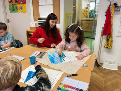 Eine Lehrerin hilft Kindern an einem Klassentisch beim Malen mit Wasserfarben.