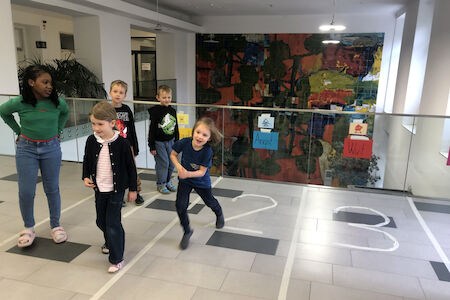 Fünf Kinder spielen und rennen drinnen auf einer mit Zahlen gefliesten Bahn um die Wette.