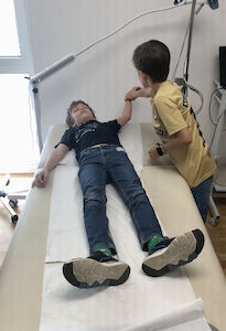 Ein Kind liegt auf einem Untersuchungstisch, während ein anderes Kind sanft seinen Arm hält.