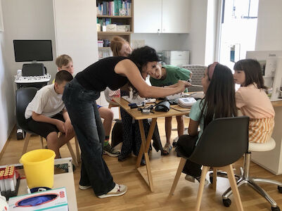 Eine Frau unterrichtet eine Gruppe von Kindern an einem Tisch in einem Klassenzimmer.