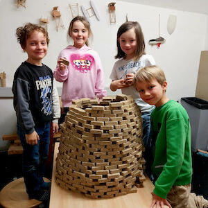Eine kleine Kindergruppe steht um einen gemauerten Turm aus Holzbauklötzen herum.