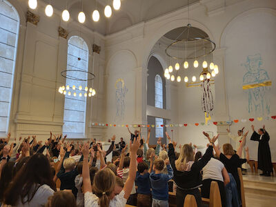 Die Schulgemeinschaft feiert in der Kirche des Augustinums eine Segensfeier und hebt dazu am Anfang die Hände in die Höhe.