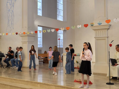Mädchen und Buben spielen ein kleine Theaterstück im Altarraum. Ein Mädchen spricht dabei mit einem Mikrofon zum Volk.