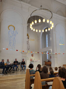 Johannes Chum hält eine Predigt. Im Hintergrund sitzt das kleine Musik-Ensemble.