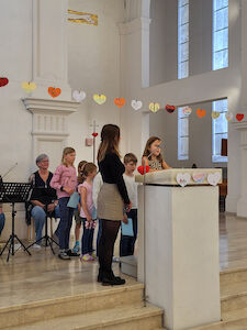 Schüler*innen verlesen die Fürbitten. Eine Studentin hilft ihnen dabei.