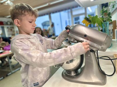 Ein Bub bedient in der Klasse die graue KitchenAid-Küchenmaschine.