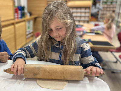 Ein Mädchen mit langen Haaren walkt gerade eine Teigkugel mit Hilfe eines Nudelwalkers aus.