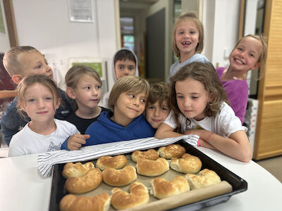 Die fertigen Kipferl liegen duftend am Backblech. Dahinter stehen neun fröhliche Kinder.