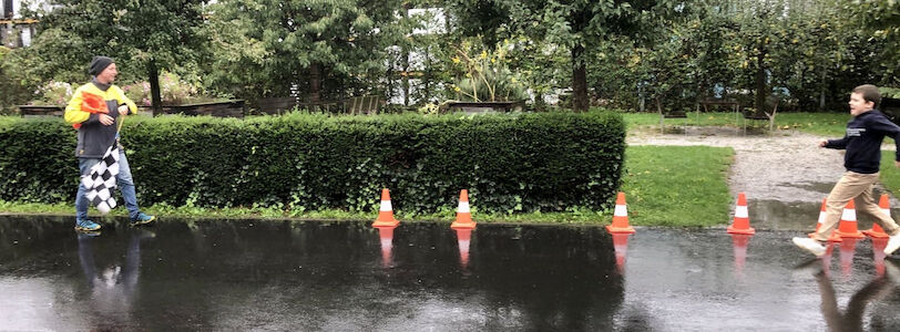 Ein Bub läuft auf einer nassen Straße am ÖAMTC-Gelände im Rahmen der Aktion "Hallo Auto" und versucht auf das Zeichen mit der Fahne, die ein Mann in Händen hält, rechtzeitig stehen zu bleiben.