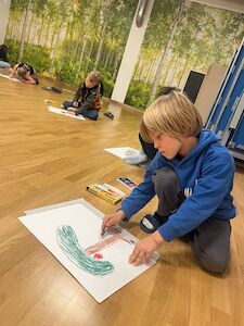 Ein Bub malt am Boden seinen "perfekten Apfel" auf ein Blatt Papier.