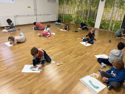 Mehrere Kinder malen am Parkettboden im Bewegungsraum ihren "perfekten Apfel".