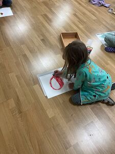 Ein Mädchen ist von hinten zu sehen, die ihren "perfekten Apfel" mit roter Farbe zeichnet.