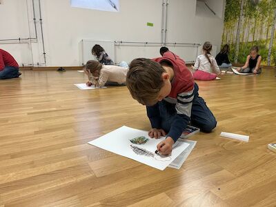 Ein Bub ist gerade dabei seinen "perfekten Apfel" zu malen und sitzt dabei am Boden.