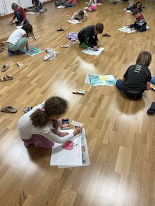 Mehrere Kinder malen am Parkettboden im Bewegungsraum ihren "perfekten Apfel".