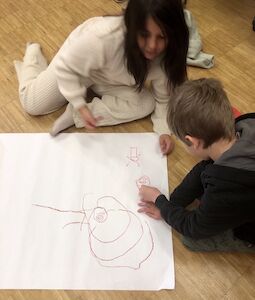 Zwei Kinder malen am Boden auf einem Plakat.