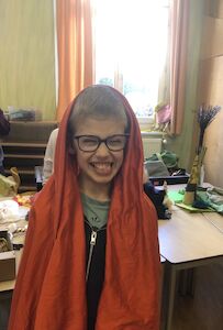 Ein Bub grinst verschmitzt in einem roten Umhang in die Kamera.