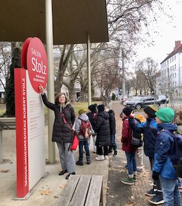 Die Klassenlehrerin der Sonnen-Klasse steht mit ihrer Klasse "stolz" vor dem Museum "Salon Stolz".