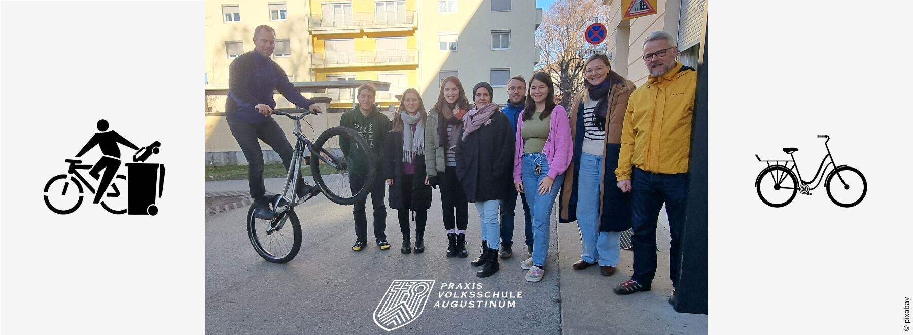 Ein Teil des Kollegiums posiert vor dem Haupteingang der Praxisvolksschule, um als "Radfahrer*in des Monats" gefeiert zu werden.