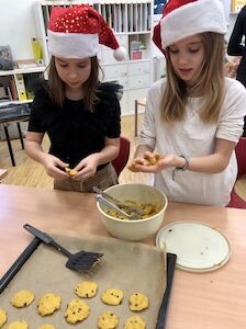 Zwei Mädchen mit einer Weihnachtsmütze formen Kekse und legen sie auf ein Backblech.