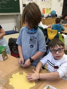 Zwei Buben stechen Kekse aus. Einer von ihnen hat eine Brille auf und sitzt.