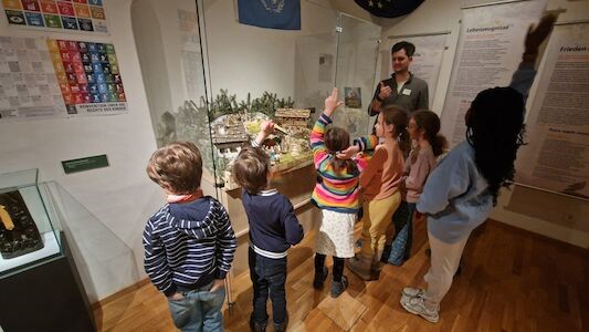 Ein kleine Kindergruppe bekommt vom Museumsführer spannende Dinge über Krippen erklärt.
