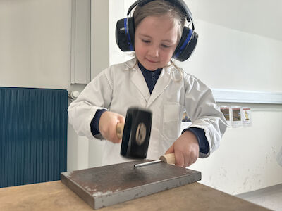 Ein Mädchen hämmert einen Metalldraht flach. Sie trägt einen Gehörschutz.