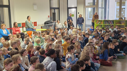 Die Kinder und Lehrer*innen der Praxisvolksschule hören gebannt bei der Schulversammlung zu.