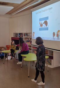 Die Podiumsdiskussion startet. Zwei Kinder sprechen mit einer Lehrerin über das Thema "Konflikte lösen".