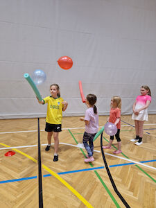 Vier Mädchen halten mit einer Schwimmnudel Luftballone in der Luft.