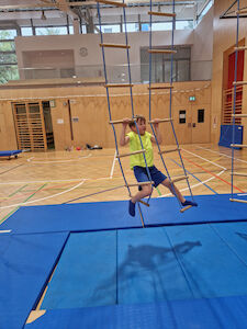 Ein Bub klettert von einer Hängeleiter zur nächsten.