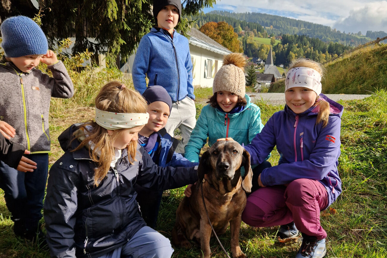 Eine kleine Kindergruppe sitzt bzw. steht um einen Hund herum und lächelt in die Kamera.