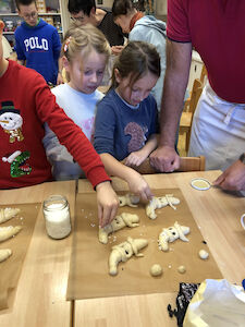 Mehrere Kinder bestreuen das Backgut mit Hagelzucker.
