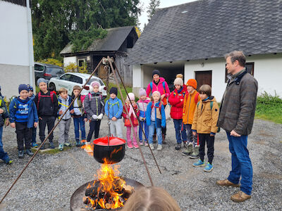 Viele Kinder stehen mit zwei Erwachsenen um ein Lagerfeuer herum.
