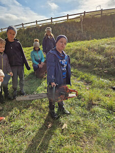 Ein Bub fühlt das schwere Gewicht einer echten Motorsäge, indem er sie hochhebt.