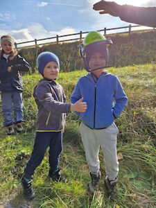 Ein Bub wird mit einem Forstarbeiterhelm ausgestattet, während ein anderer Bub daneben steht.