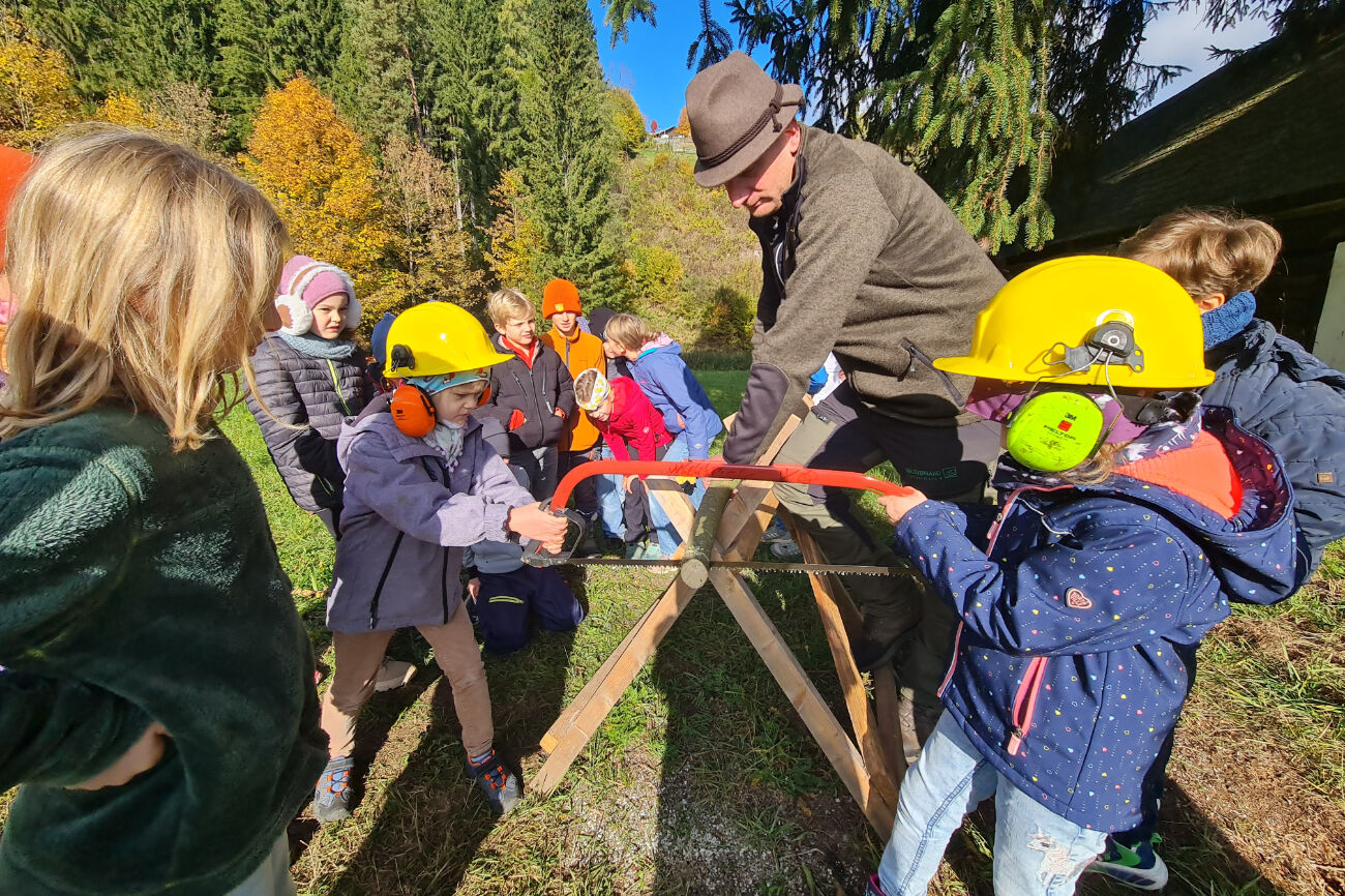 Zwei Kinder sägen gemeinsam mit Schutzausrüstung einen dicken Ast ab.