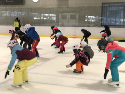 Die Kinder fahren am Eis und gehen dabei in die Hocke.