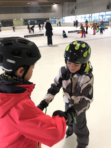 Im Vordergrund geben sich zwei Buben die Hände probieren zu fahren während im Hintergrund viele andere Kinder zu sehen sind.