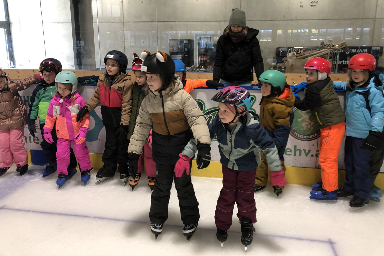 Eine Kindergruppe versucht sich am Eis und wartet auf die Anweisungen des Trainers.