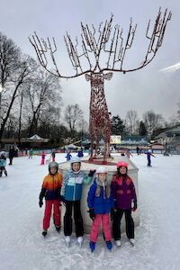 Vor einer metallenen Hirschskulptur in der Grazer Winterwelt posieren vier Kinder am Eislaufplatz für ein Foto.