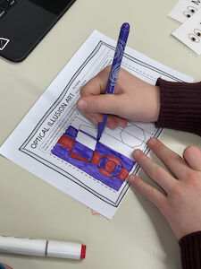 Ein Kind malt eine optische Illusion mit Filzstiften aus.