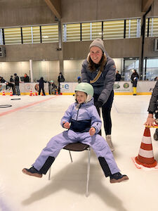 Eine Lehrerin fährt mit einem Mädchen am Stuhl freudig übers Eis.