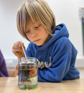 Ein Bub mischt Wasser mit Öl in einem Glas und beobachtet, was dabei passiert.