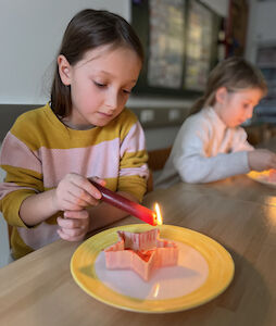 Ein Kind experimentiert mit einer roten Kerze über einem Porzellanteller, worauf ein Stern steht.