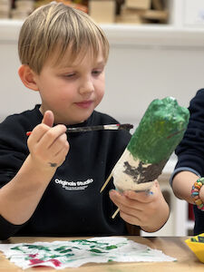 Ein Bub malt seine selbstgebaute Rakete mit Temperafarben an.
