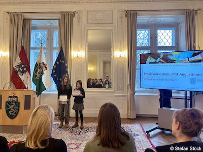 Zwei Mädchen vom Schulrat beim Präsentieren neben einem großen TV-Gerät.