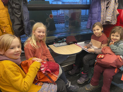 Eine Mädchengruppe sitzt im Zug und lächelt in die Kamera.