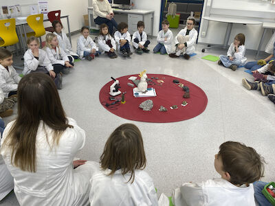 Im Lehr-Lern-Labor treffen sich die Kinder am Anfang in einem Kreis um einen roten Teppich mit vielen Gegenständen.